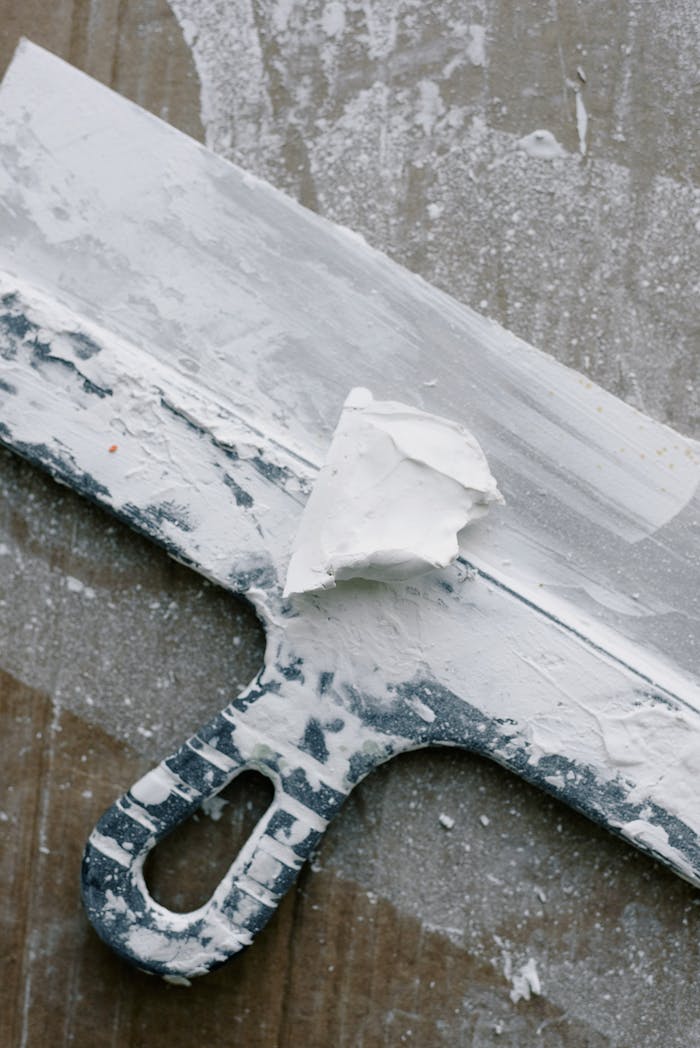 From above of spatula in dust and plaster on wooden table during renovation