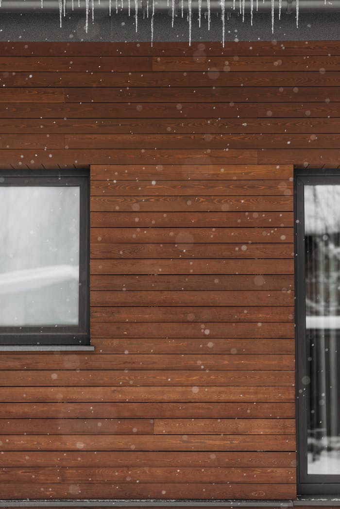 Close-up of a wooden house wall with snowflakes falling and icicles hanging.